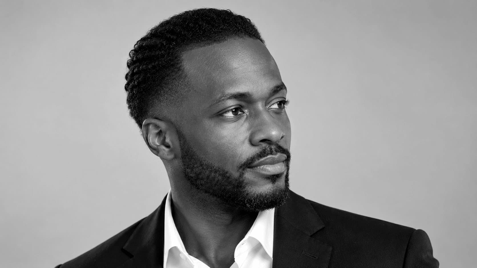 Homme aux cheveux courts coiffés vers l’arrière, front dégagé, en chemise blanche et veste noire